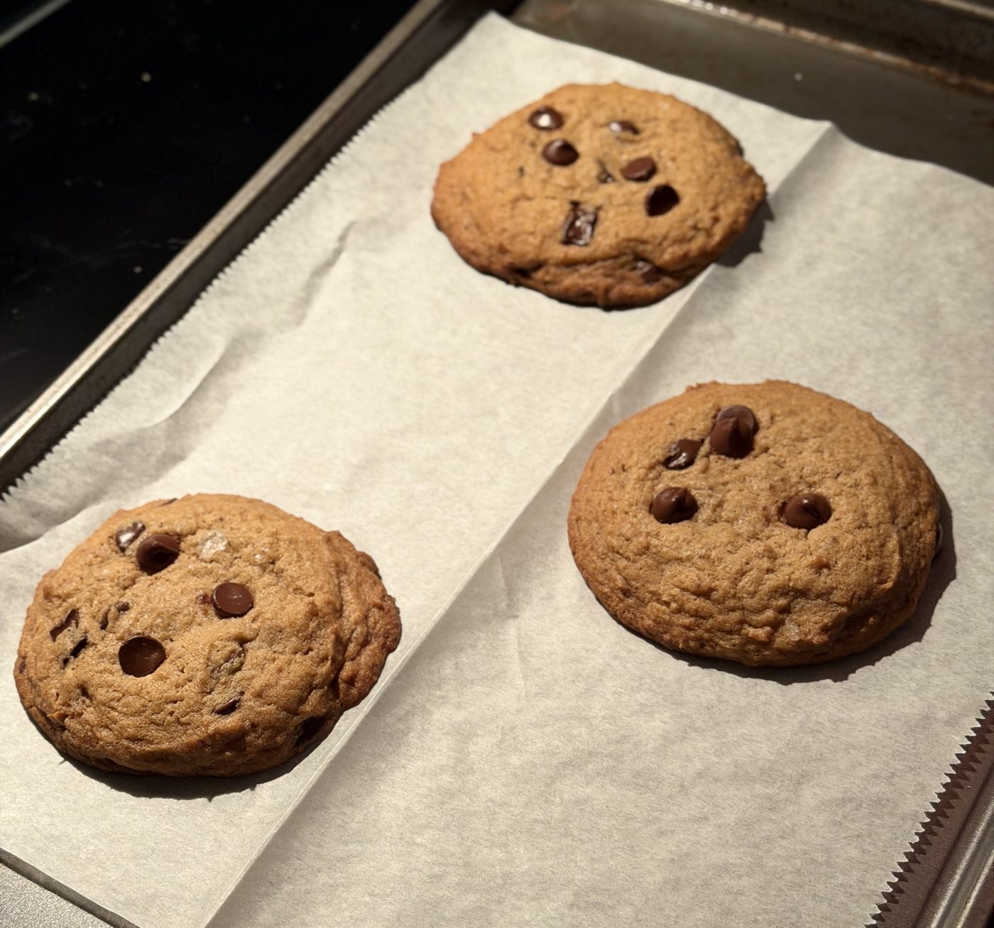 Three baked cookies on parchment, thick and domed with a rolled edge